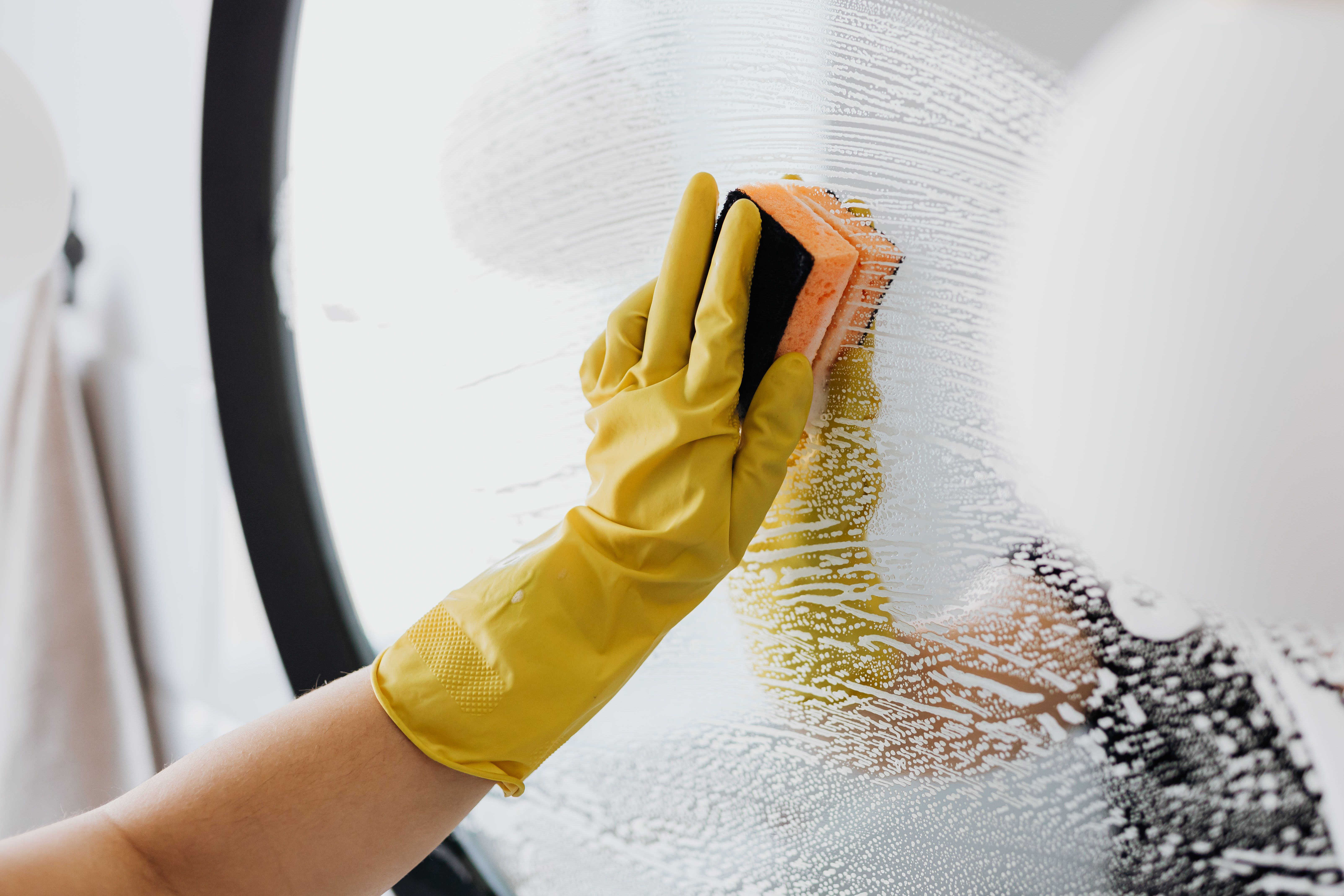 hand in yellow rubber glove sponging a mirror