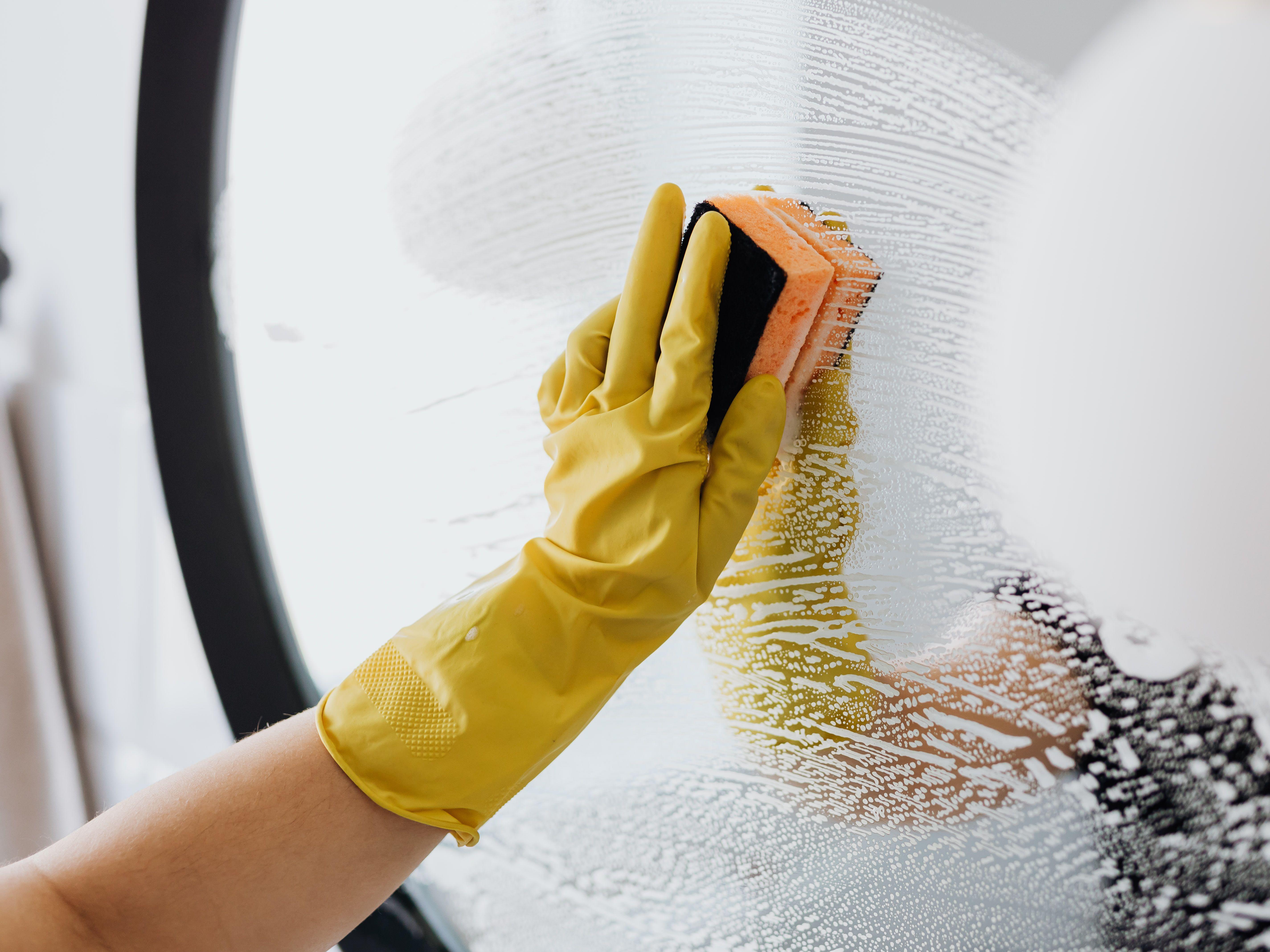 hand in yellow rubber glove sponging a mirror